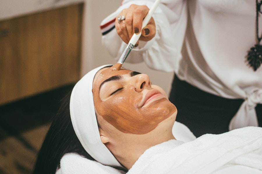 An aesthetician applying a clay mask to a client's face with a brush