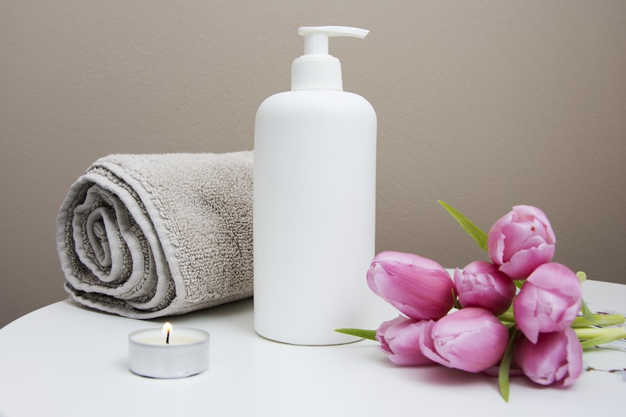 A rolled towel, lotion, candle, and pink tulips on a spa side table